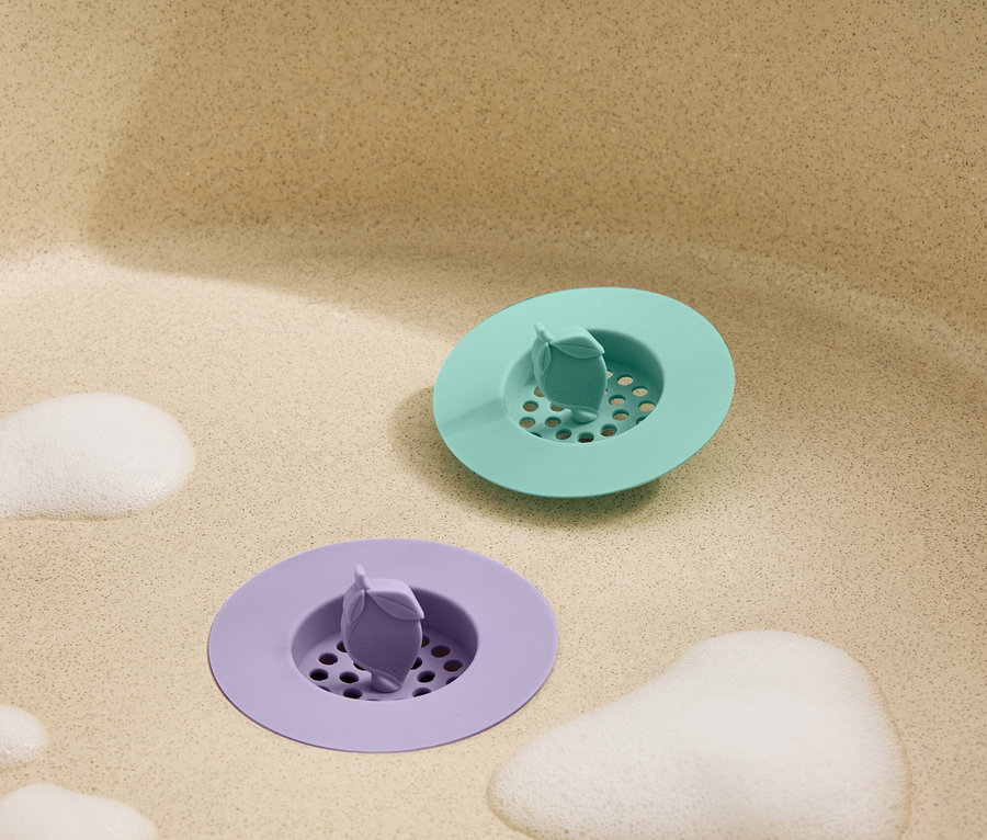 Vue de dessus d'un bouchon d'évier vert et violet avec de la mousse dans un évier beige.