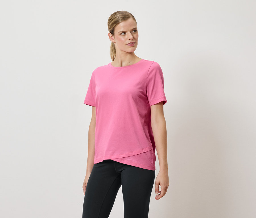 Femme posant dans un t-shirt rose et un pantalon noir.