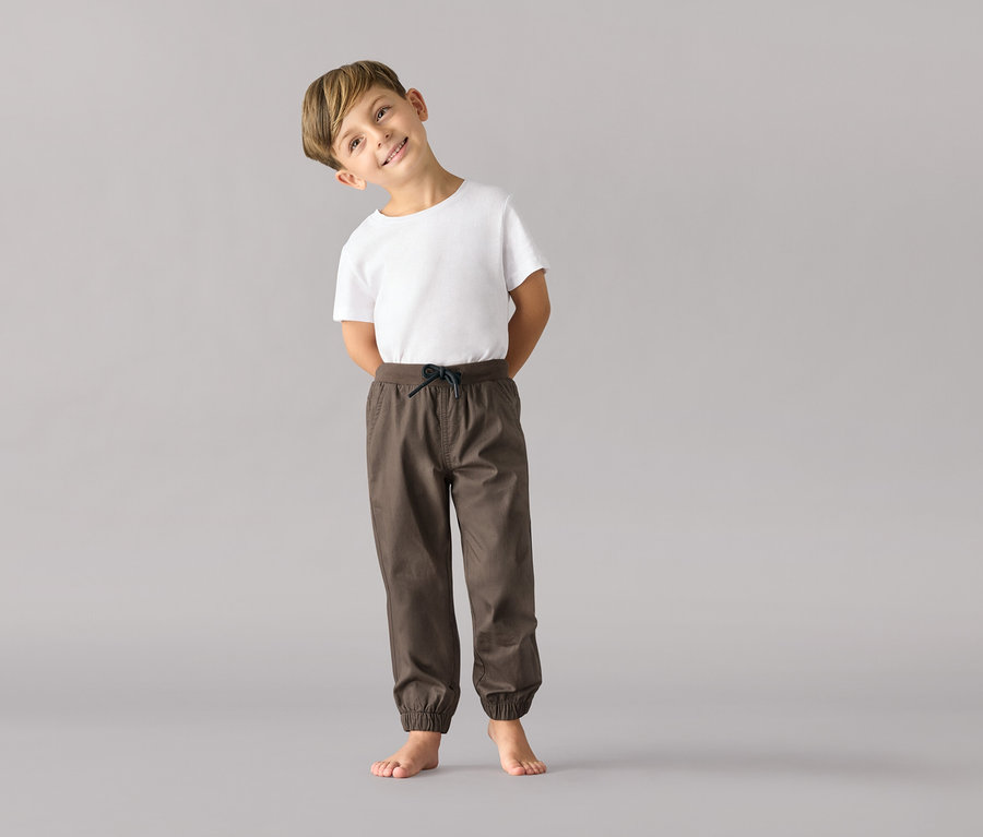 Un garçon portant un t-shirt blanc et un pantalon à enfiler pour enfants – Coupe « Anton » se tient pieds nus sur un fond gris.