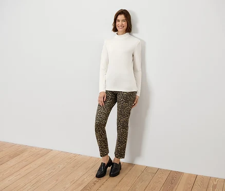 Femme posant portant un haut crème à manches longues et un pantalon imprimé animal.