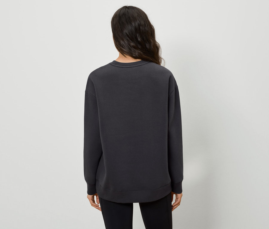 Vue de dos d'une femme aux cheveux foncés portant un pull noir et un pantalon noir.