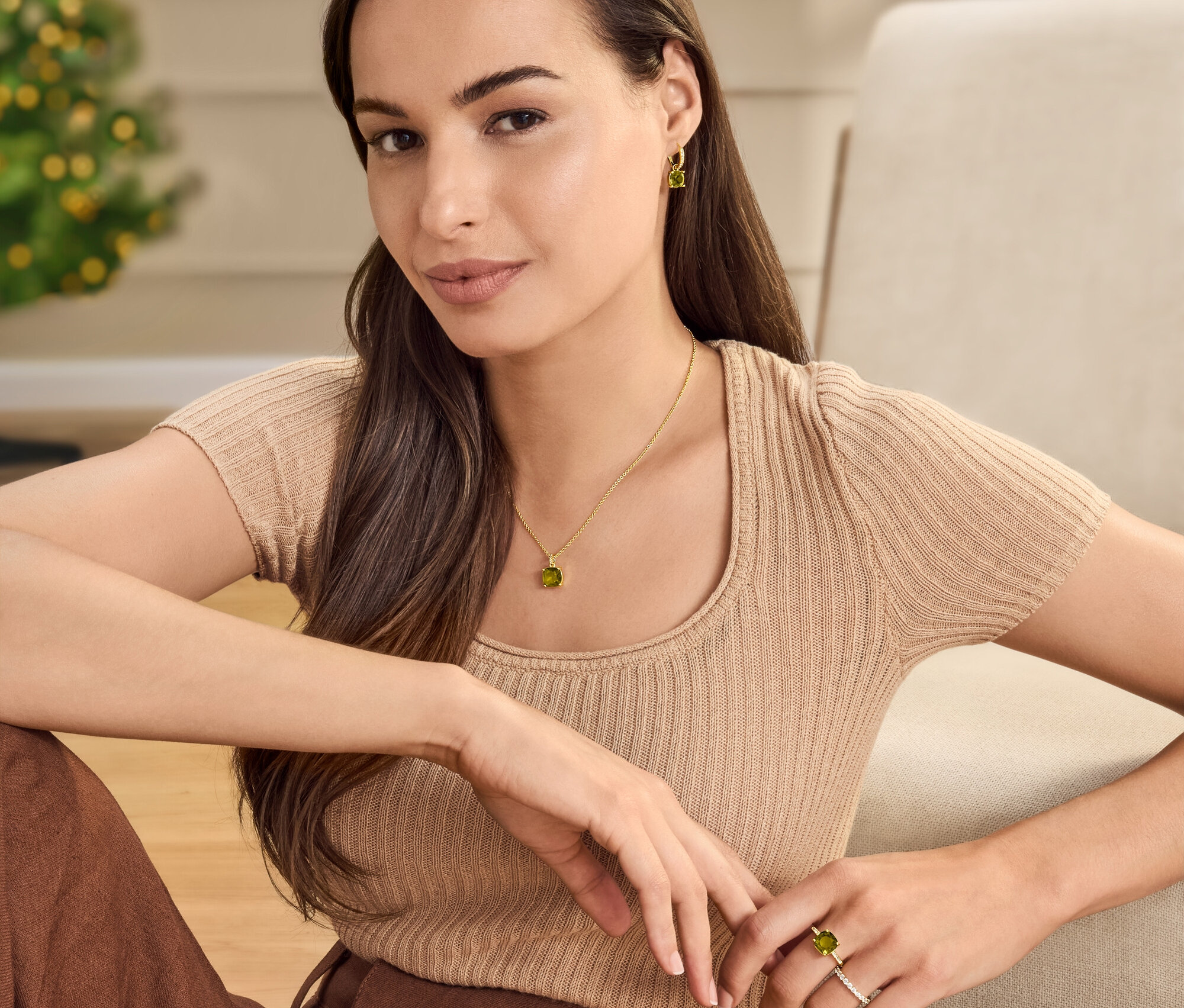 Femme assise portant chaîne, créoles et bague avec cristal de verre vert-marron. Elle porte également un anneau argent 925 « Memory », doré.