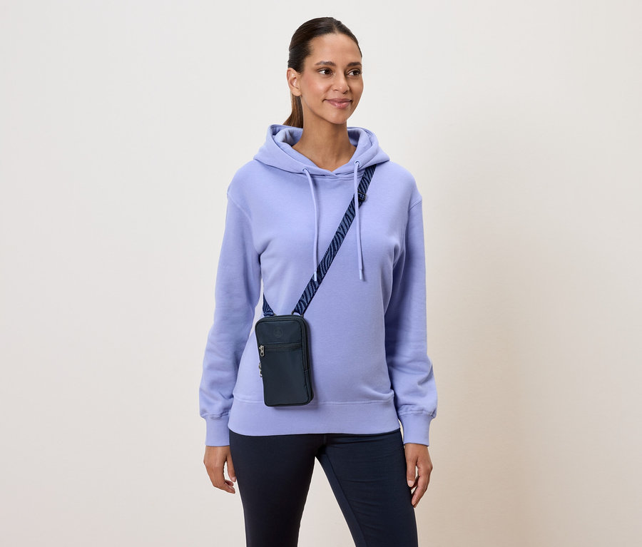 Une femme portant un sweat à capuche violet clair et un sac bandoulière bleu marine.