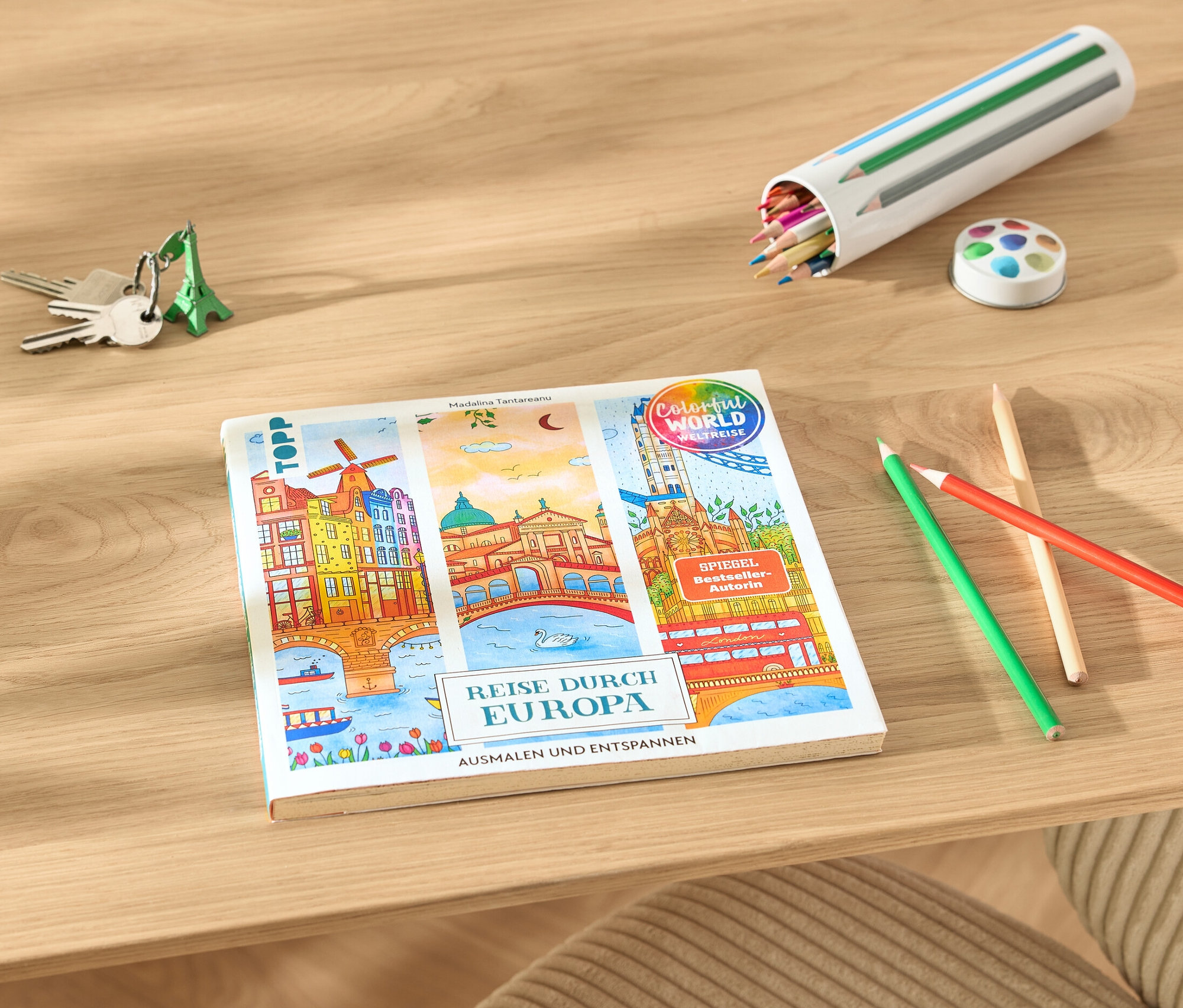 Sur une table sont posés le livre « Reise durch Europa – Ausmalen und Entspannen », des crayons de couleur et des clés.