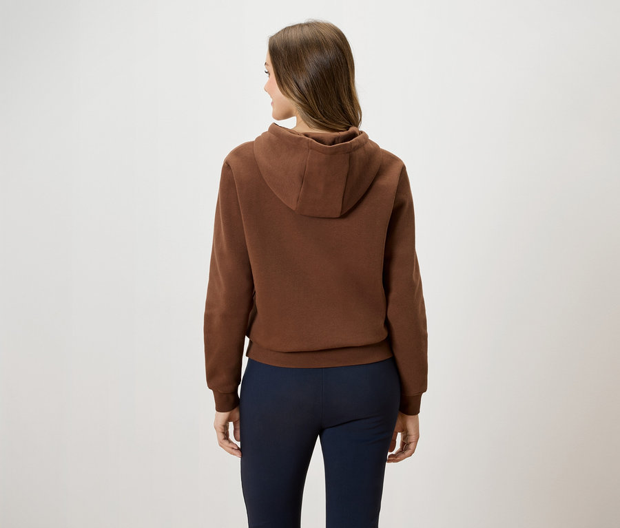 Vue arrière d'une femme aux cheveux bruns portant un sweat à capuche marron et un pantalon bleu foncé.
