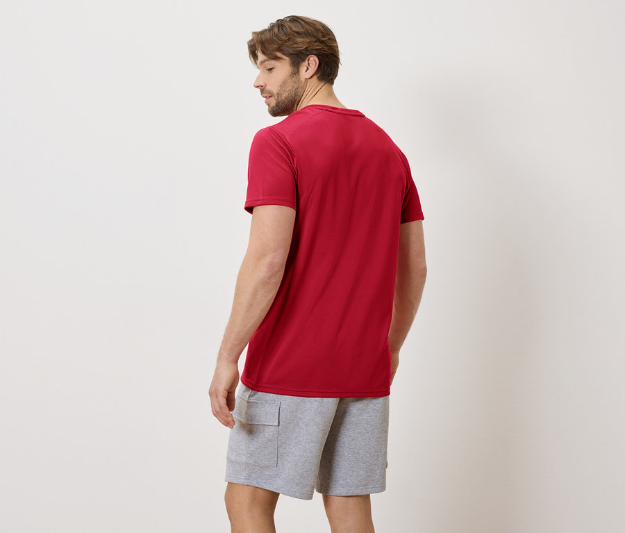 Homme vu de dos portant un t-shirt rouge et un short gris sur un fond neutre.