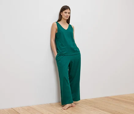 Une femme est appuyée contre un mur et porte un débardeur vert et un pantalon assorti.