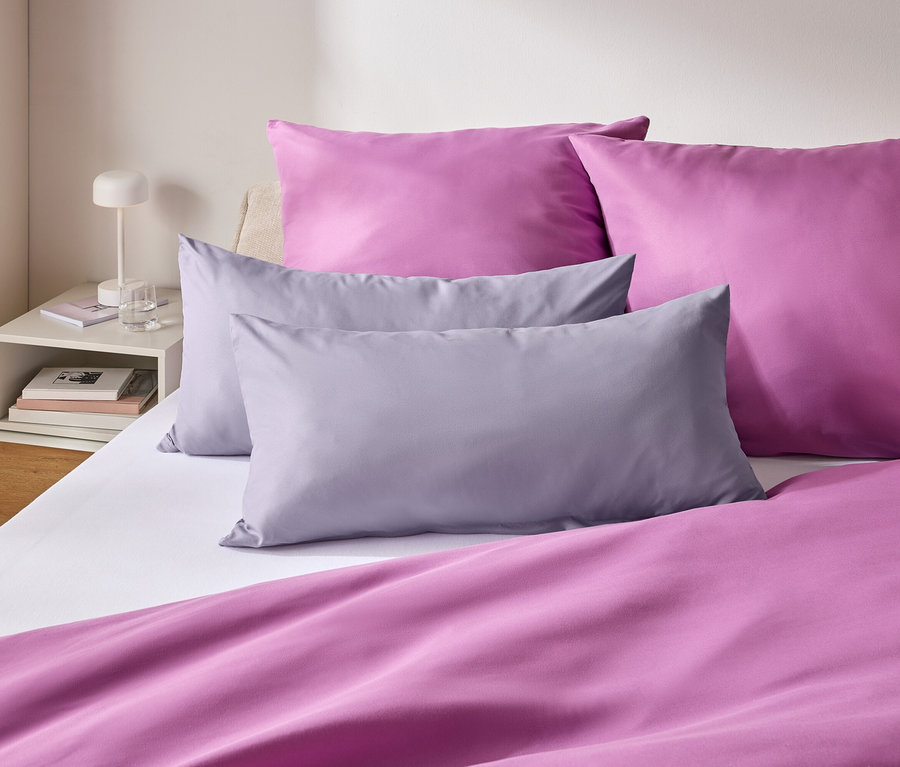 Gros plan d'un lit avec des draps violets et des coussins violets et gris.