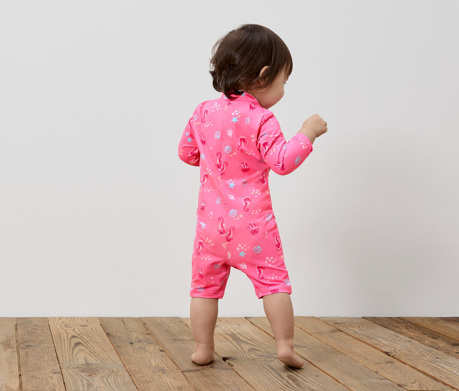 Petit enfant vu de dos, portant un maillot de bain rose avec un motif d'hippocampes.