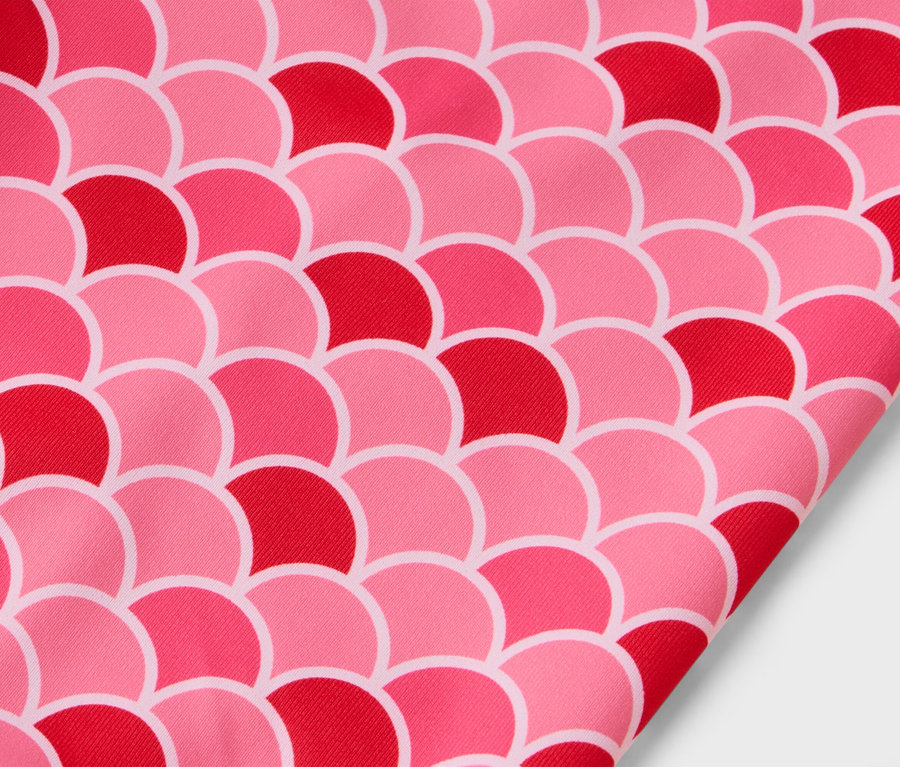 Gros plan d'un tissu avec un motif d'écailles roses et rouges.