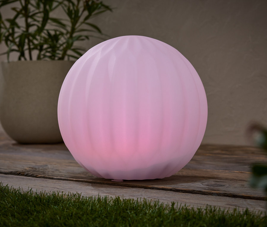 Une lampe sphérique rose est posée sur une table en bois, à côté d'un pot de fleurs contenant une plante.