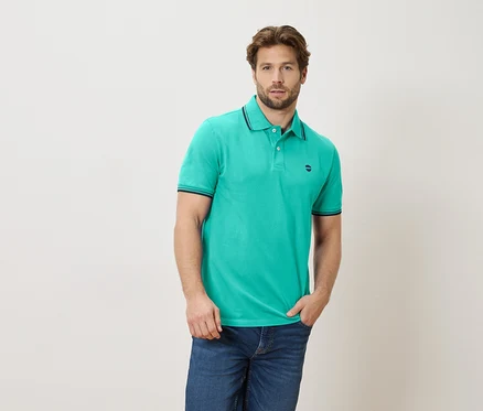 Homme portant un polo vert émeraude et un jean, une main dans la poche.