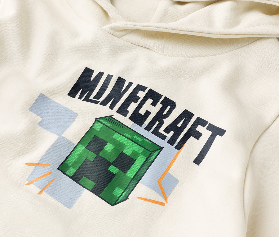Vue détaillée d'un sweat à capuche crème avec l'inscription "Minecraft" et un bloc Creeper vert.