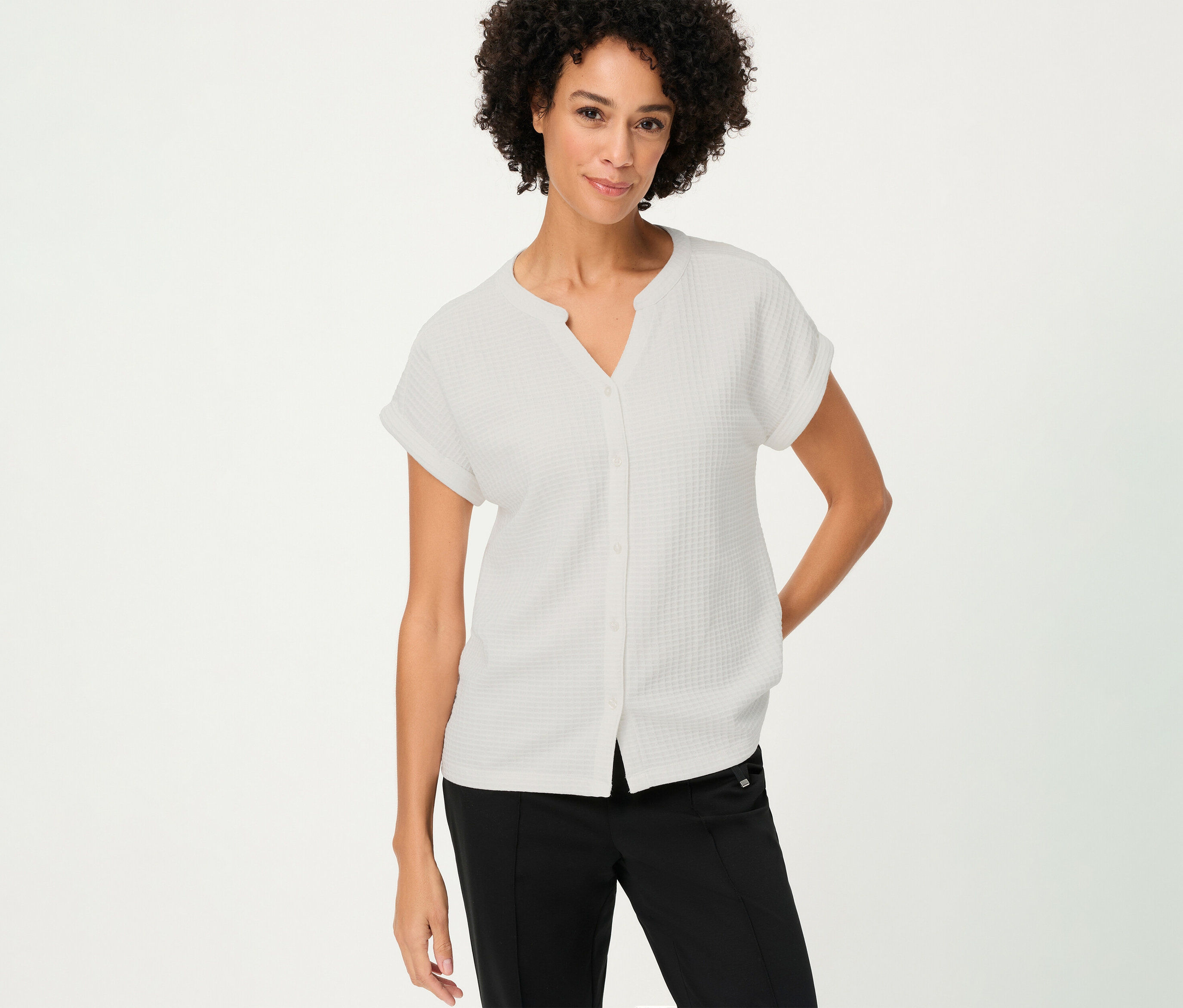 Une femme aux cheveux bouclés porte un t-shirt Olsen structuré avec boutons blanc et un pantalon noir.