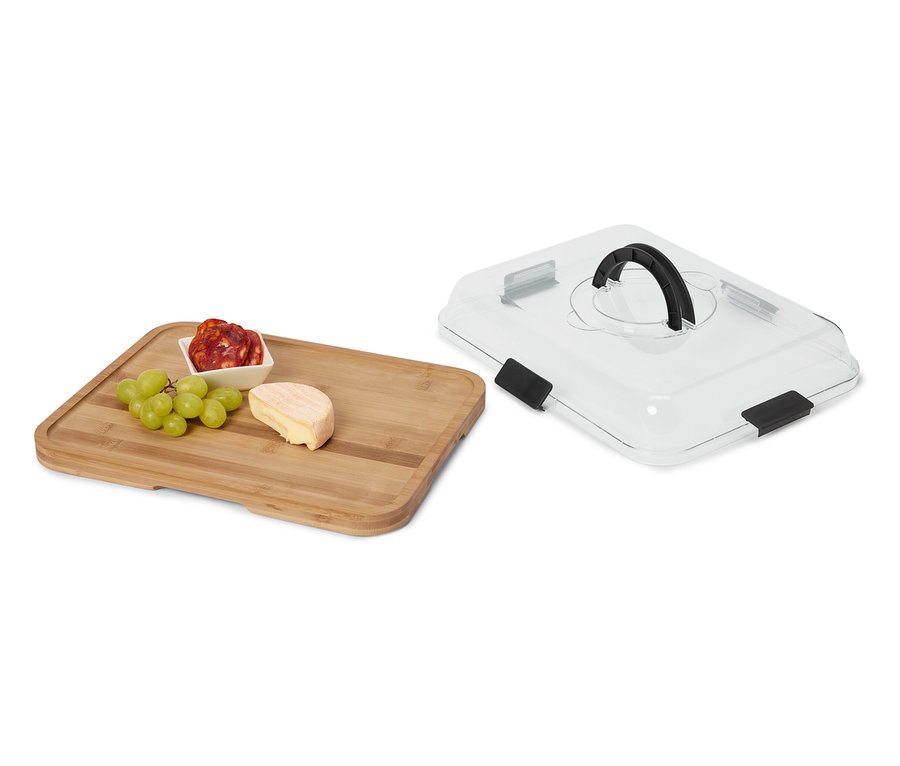Fromage, saucisson et raisins sur une planche en bois à côté d'un couvercle de service transparent avec une poignée noire.