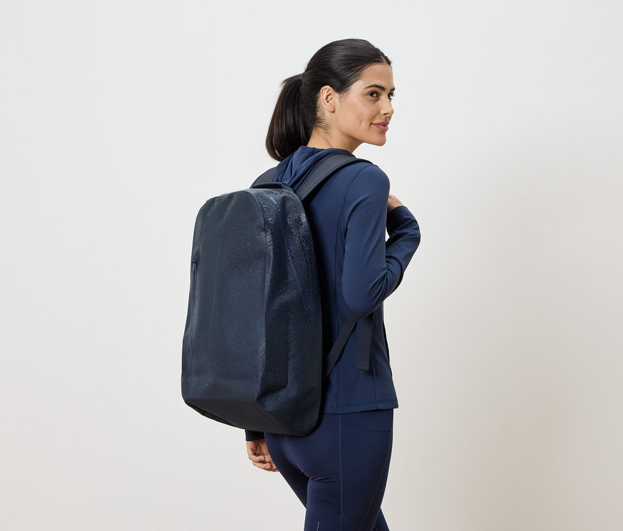 Une femme en survêtement bleu marine avec un sac à dos bleu marine sur l'épaule regarde par-dessus son épaule.