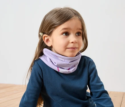 Une fille aux cheveux bruns avec une barrette porte un T-shirt bleu à manches longues et un foulard violet à motif de licorne.
