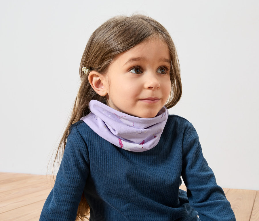 Une fille aux cheveux bruns avec une barrette porte un T-shirt bleu à manches longues et un foulard violet à motif de licorne.