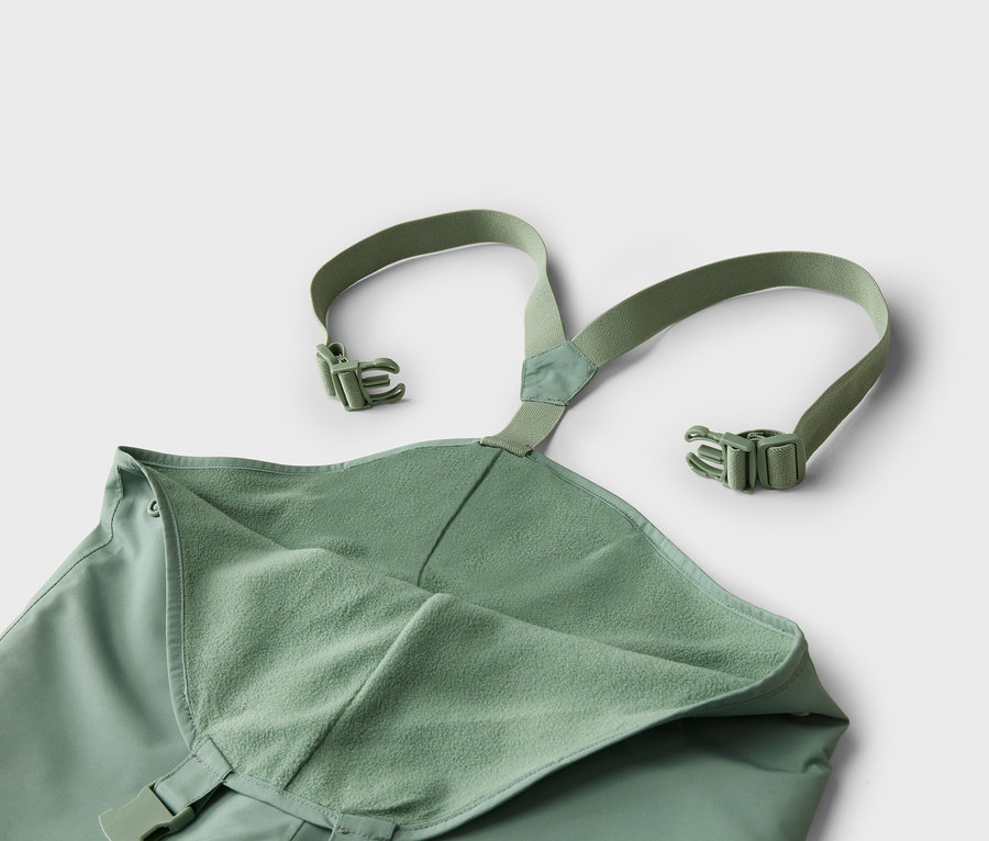 Gros plan d'une salopette de pluie verte avec des bretelles et des boucles sur fond blanc.