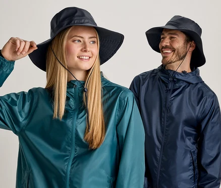 Une femme blonde et un homme barbu portent des chapeaux bleus et des vestes de pluie sur fond clair.
