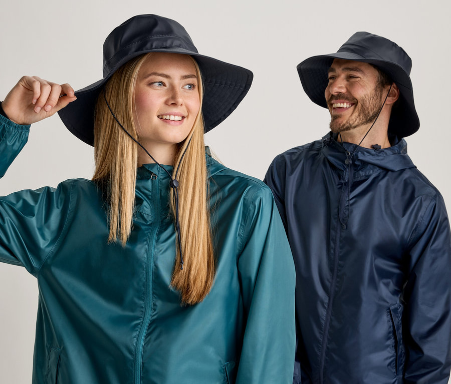 Une femme blonde et un homme barbu portent des chapeaux bleus et des vestes de pluie sur fond clair.