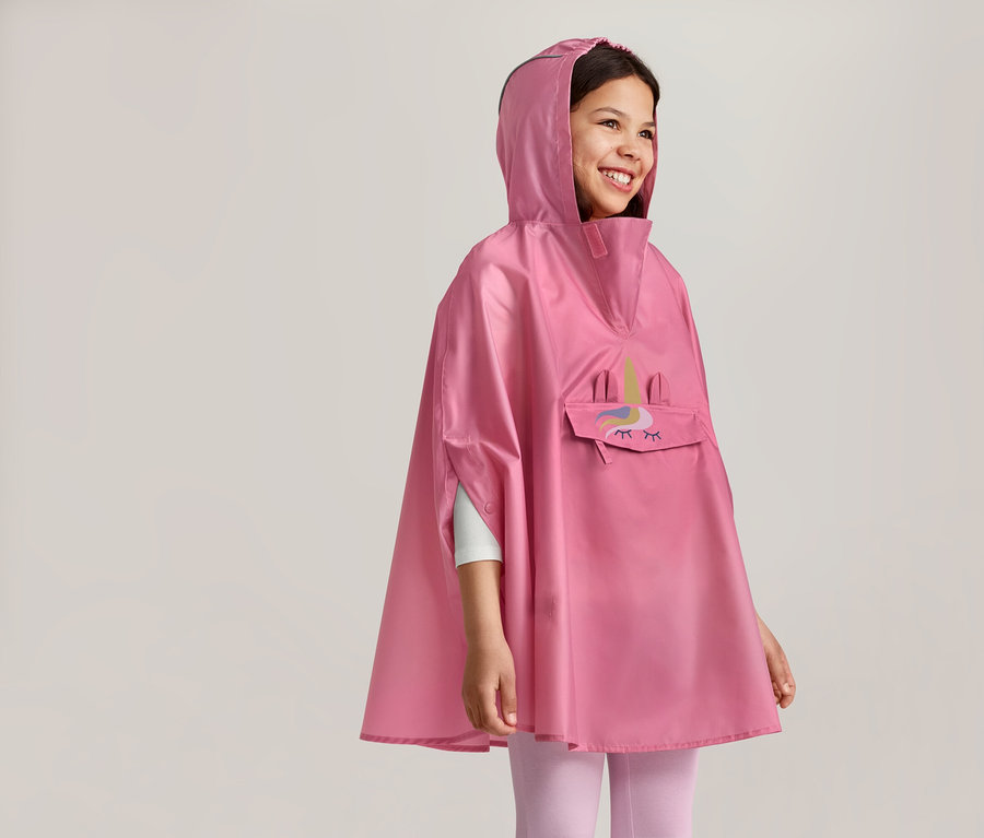 Une fille souriante à capuche porte un poncho rose avec un motif de licorne et une poche sur le devant.