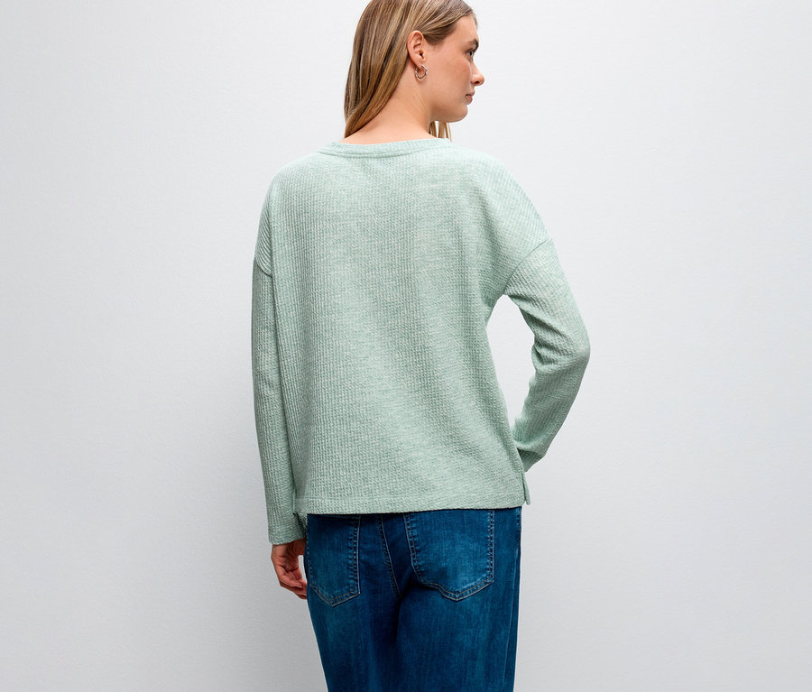 Vue arrière d'une femme aux cheveux blonds portant un maillot avec structure Street One et un jean bleu.