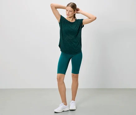 Femme posant en t-shirt vert foncé et short, portant des baskets blanches.
