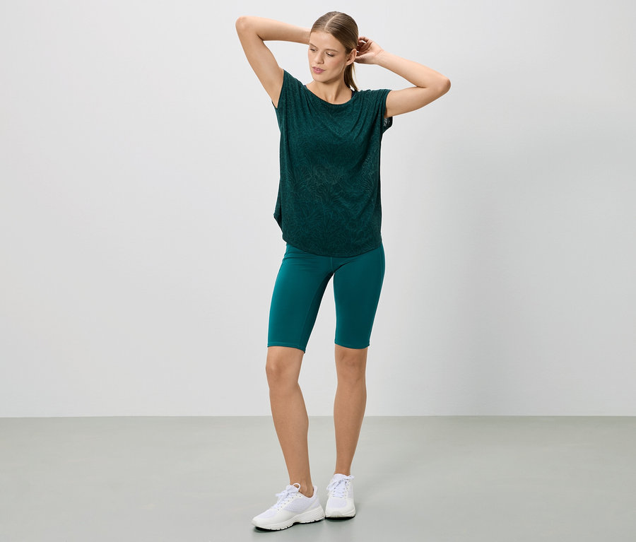 Femme posant en t-shirt vert foncé et short, portant des baskets blanches.