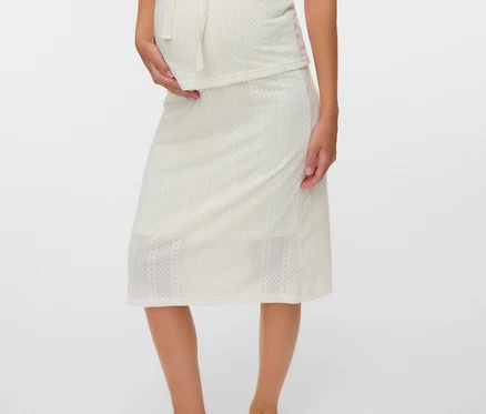 Une femme enceinte porte un ensemble deux pièces à motifs de couleur crème composé d'un débardeur à nœud et d'une jupe. Elle porte des tongs marron.