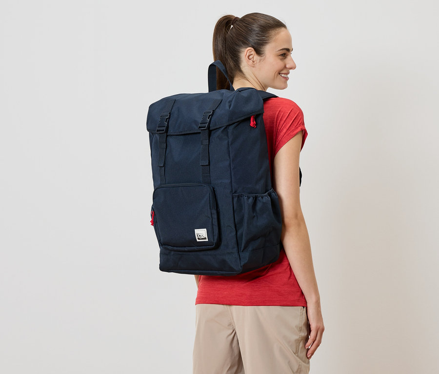 Une femme porte un sac à dos bleu marine avec des détails rouges.