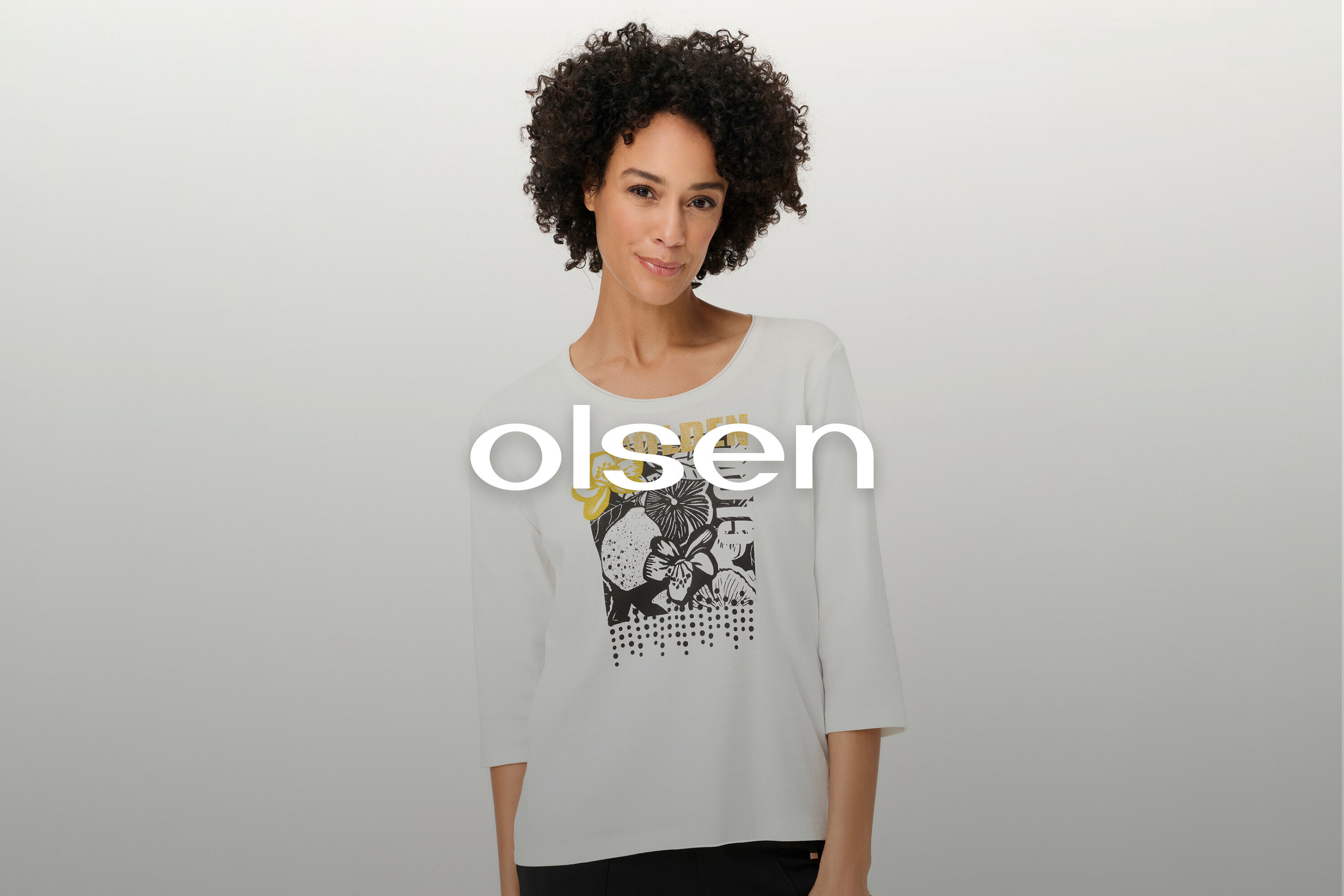 Une femme aux cheveux bouclés porte un t-shirt blanc à manches longues avec un motif floral.