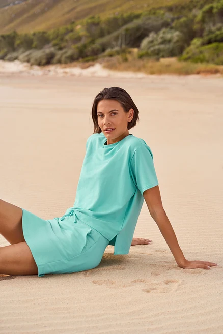 Femme assise sur la plage portant un t-shirt et un short bleu clair.