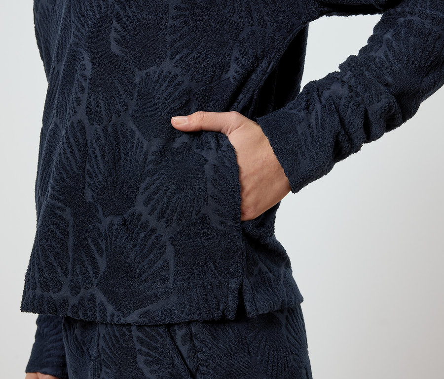 Une personne met sa main dans la poche d'un pull bleu marine à motif de feuilles.
