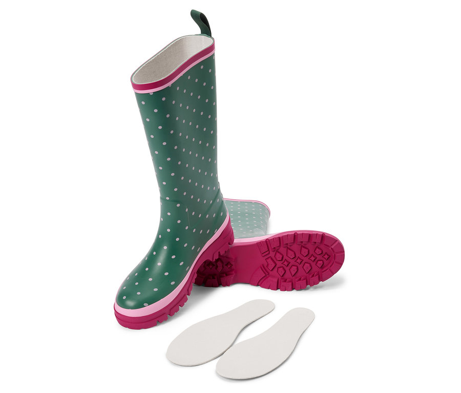Une paire de bottes en caoutchouc vertes à pois blancs couchées sur le côté, à côté des semelles intérieures blanches.