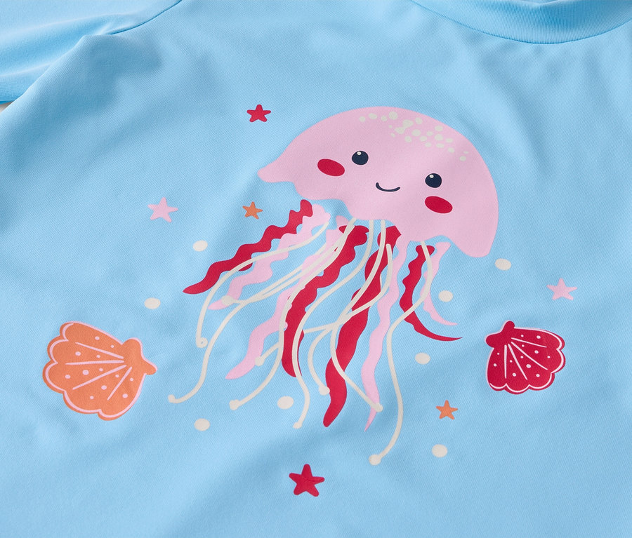 Gros plan sur un tissu bleu clair avec un imprimé de méduse rose, entouré de coquillages et d'étoiles de mer.