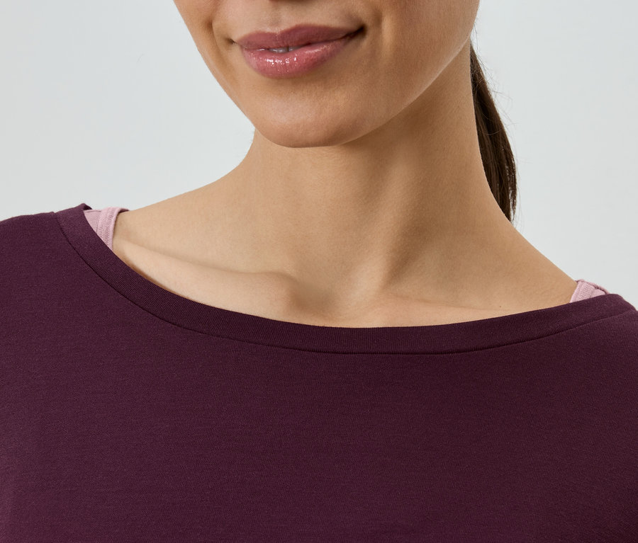 Gros plan d'une femme portant un haut bordeaux avec un débardeur rose en dessous.