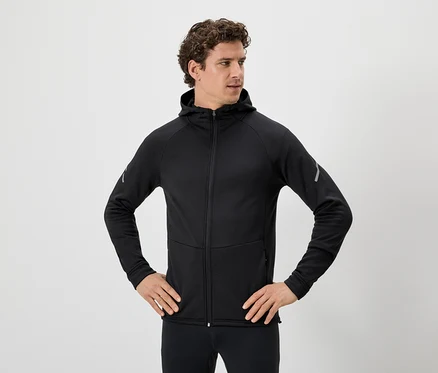 Homme aux cheveux bouclés portant un sweat à capuche noir zippé et un legging noir, les mains sur les hanches.