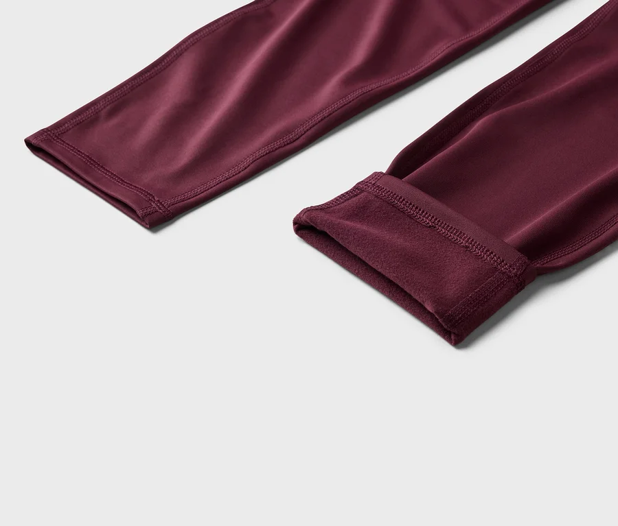 Gros plan sur un legging bordeaux, une jambe retroussée pour montrer la doublure polaire.