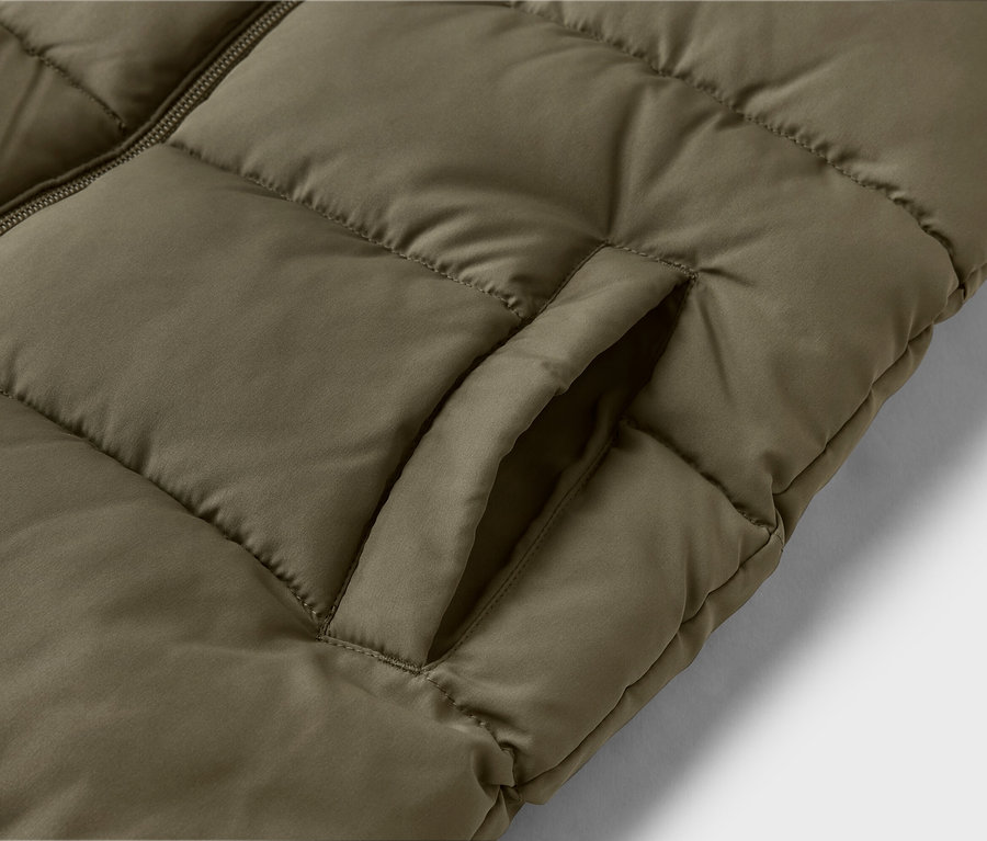 Gros plan d'un gilet matelassé vert olive avec fermeture éclair et poche ouverte.