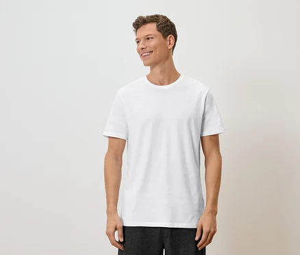 Un homme aux cheveux châtain clair et portant un t-shirt blanc regarde vers la droite.