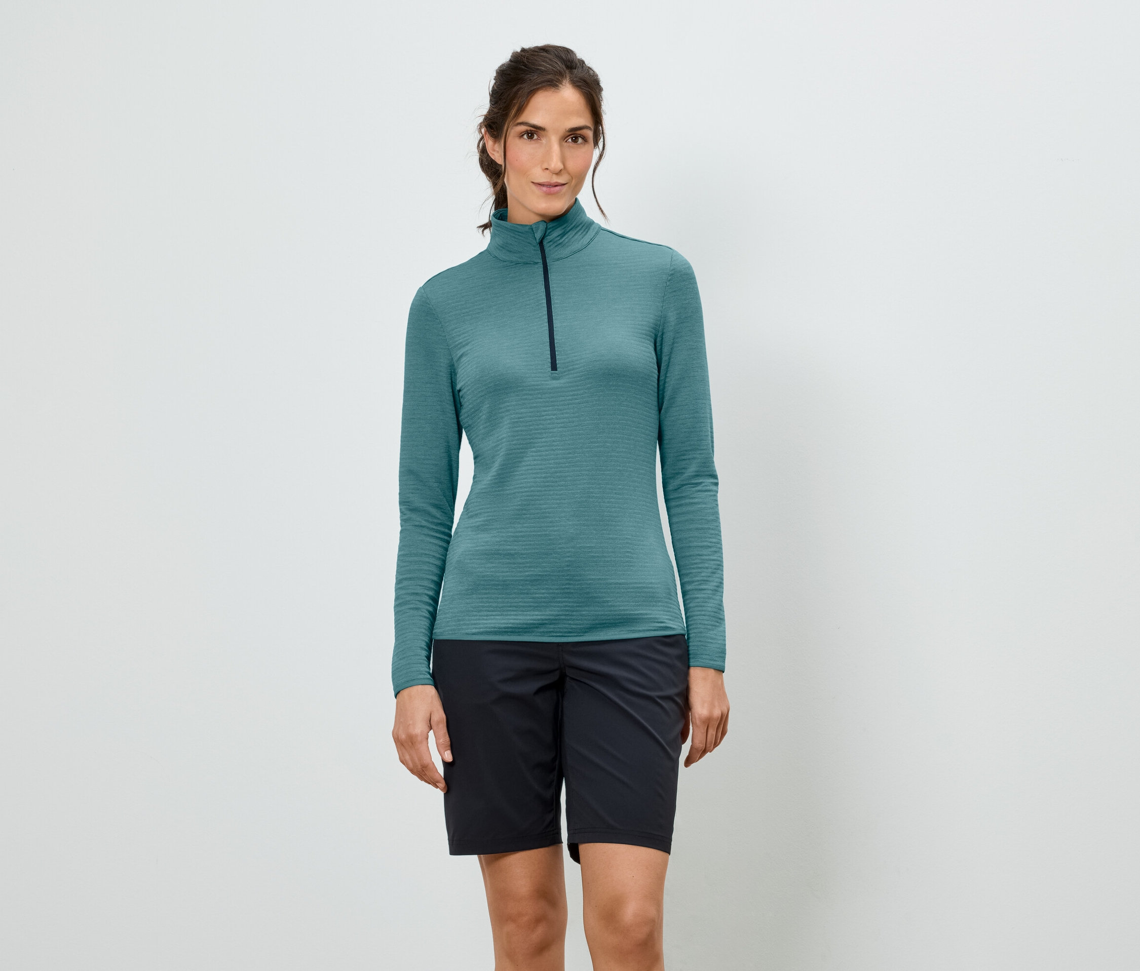 Femme portant un T-shirt turquoise à manches longues avec fermeture éclair et un short noir.