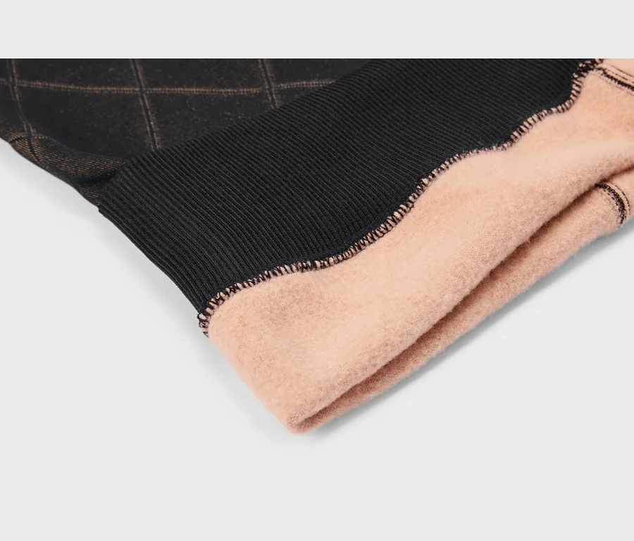 Gros plan d'un vêtement avec un poignet côtelé noir, un tissu marron foncé à motif losanges et une doublure polaire rose.