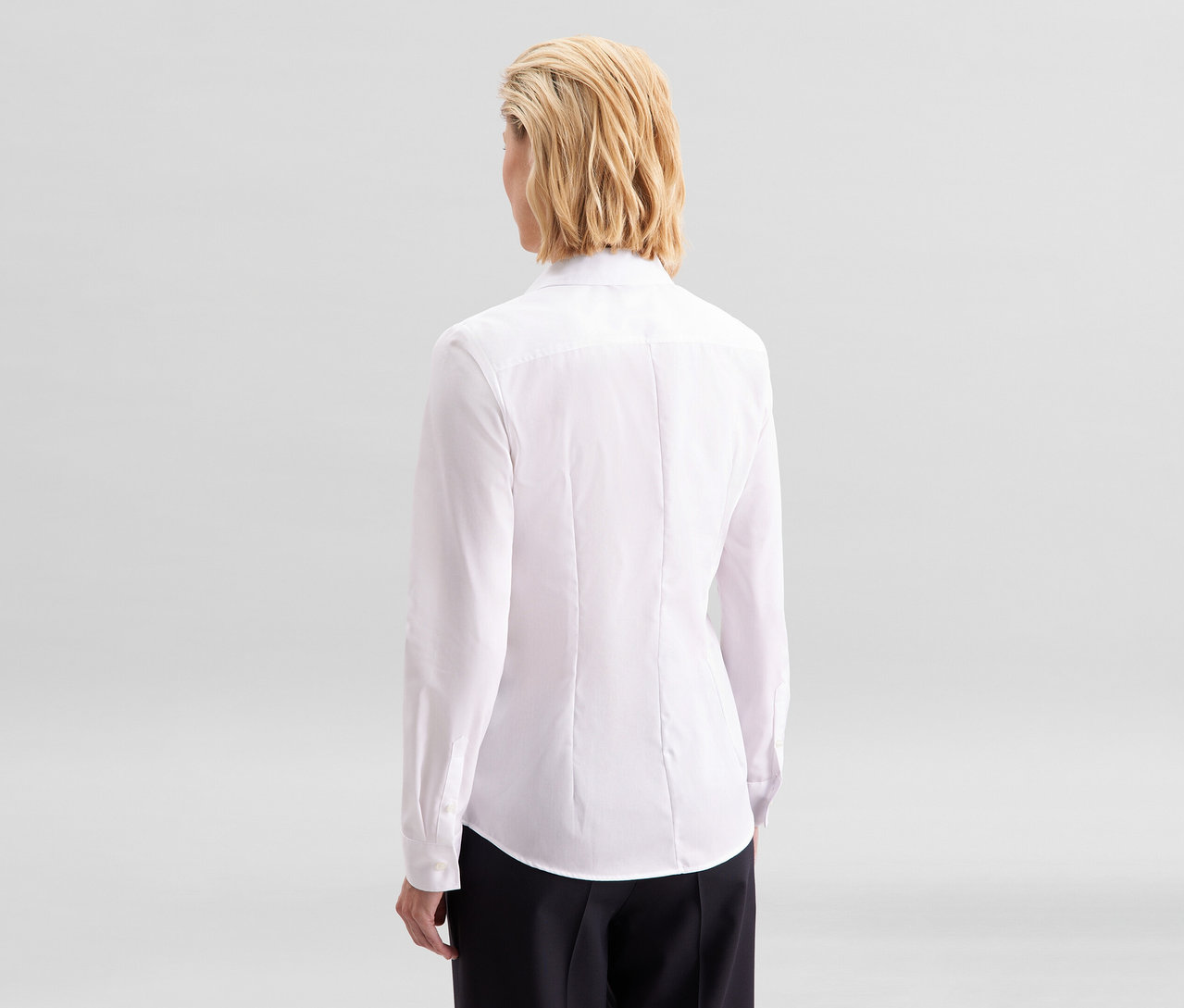 Femme vue de dos, portant un chemisier Slim Fit non iron Seidensticker blanc et un pantalon noir.