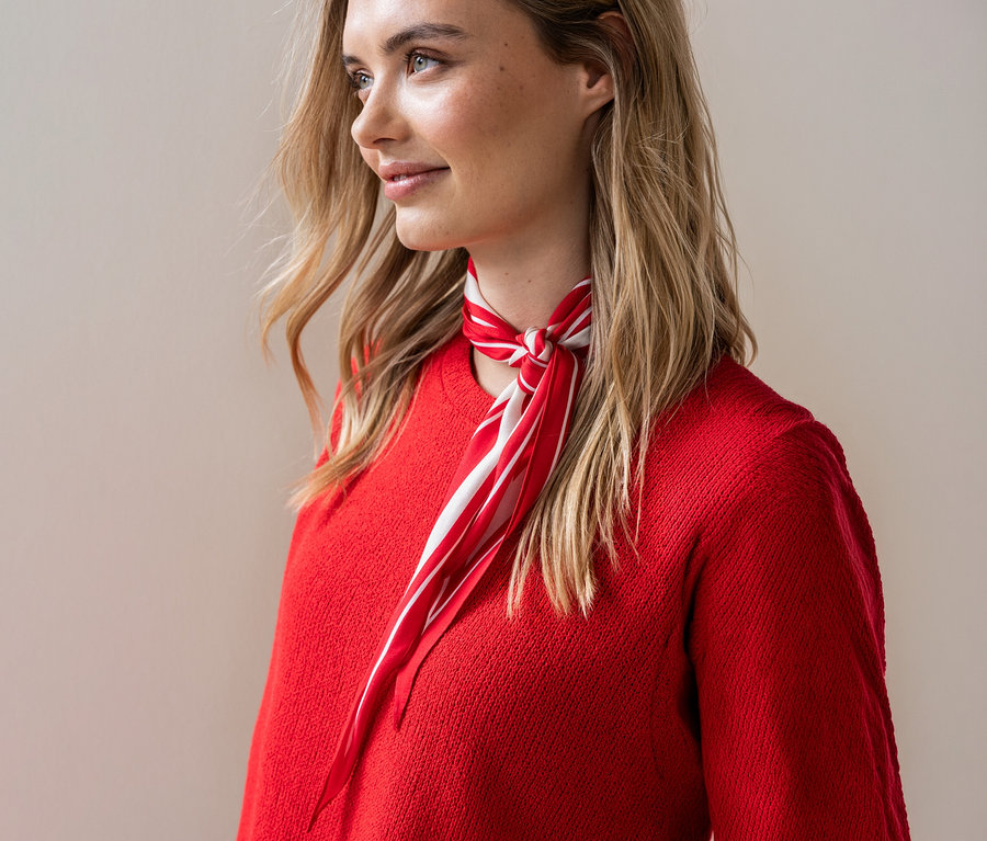 Une femme blonde portant un pull rouge noue un foulard rouge et blanc.