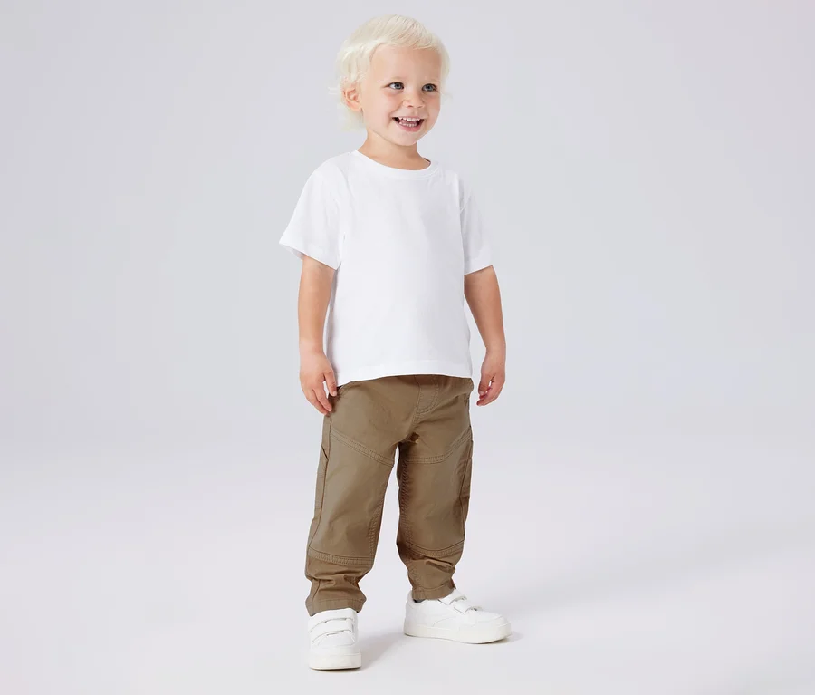 Garçon souriant portant un t-shirt blanc, un pantalon en sergé kaki NAME IT et des chaussures blanches.