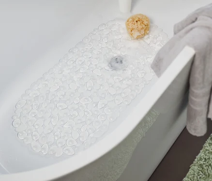 Un tapis de baignoire transparent est posé dans la baignoire. Une serviette grise est suspendue au bord de la baignoire et un tapis vert est posé à côté de la baignoire.