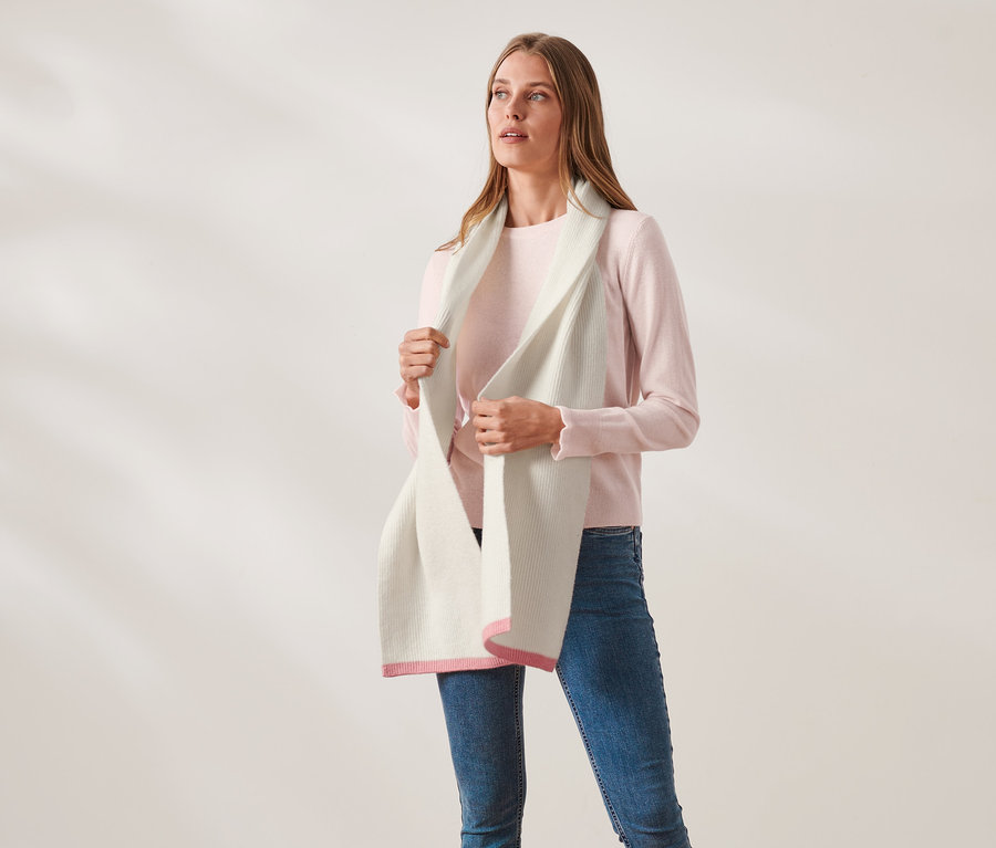Femme tenant une écharpe en maille avec de la laine de couleur crème avec des extrémités roses.