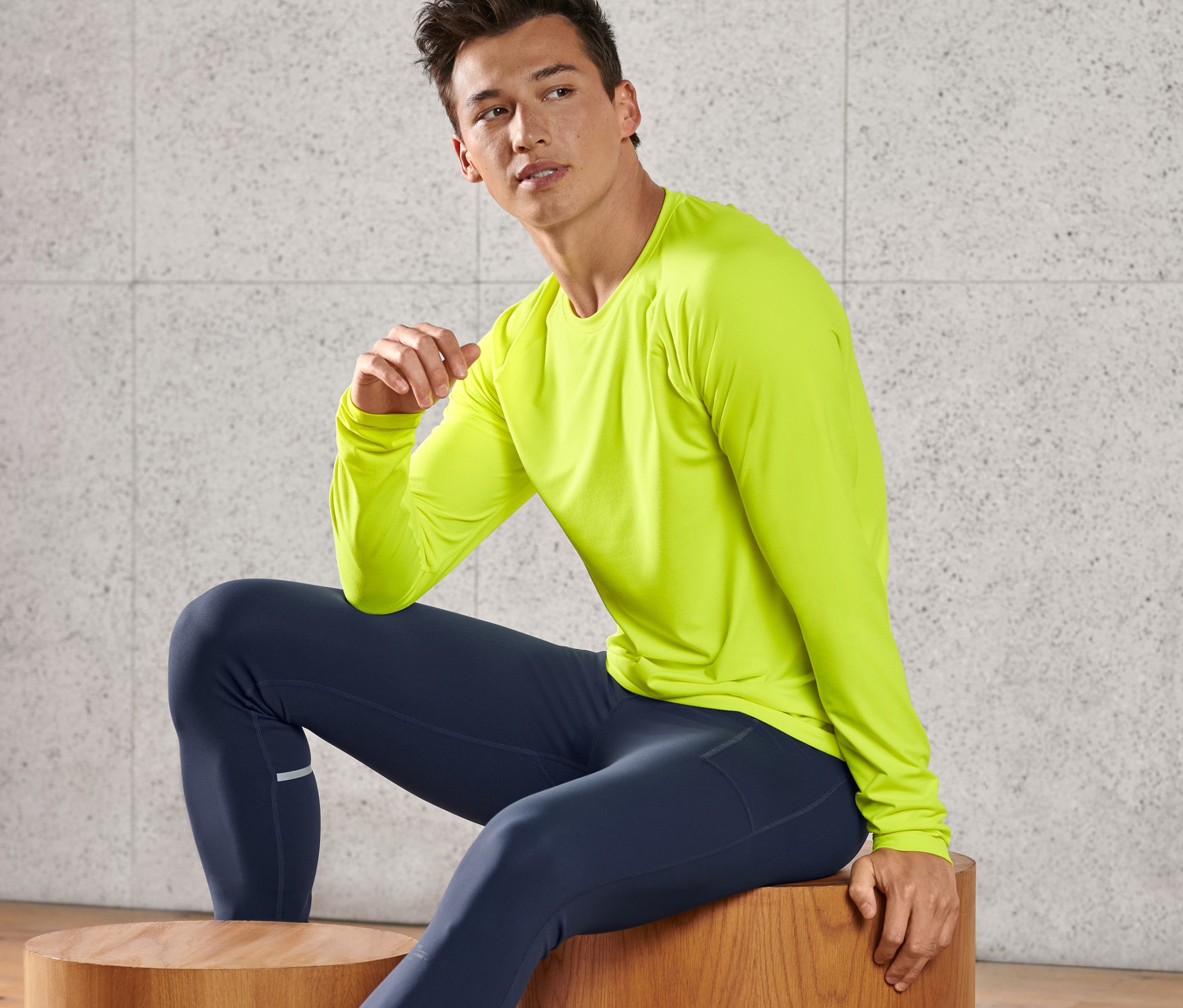 Un homme est assis sur un tabouret en bois et porte un t-shirt fonctionnel jaune fluo à manches longues.