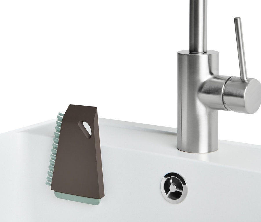 Une brosse de cuisine universelle repose à côté d'un robinet en acier inoxydable dans un évier blanc.